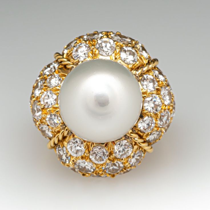 This magnificent cocktail ring is centered with one (1), post set, cultured South Sea pearl. The pearl tops a domed setting is bead set sixty-four (64), bead set, round brilliant cut diamonds. The ring has a split shank design and is accented with seven (7), bead set, round brilliant cut diamonds on each side. The ring measures 21.7mm at the top, rises 18.6mm above the finger, tapering to 2.4mm wide and 1.1mm thick at the base of the shank. The ring is currently size 7. Elegant White Domed Rings, Elegant White Domed Jewelry, White Pearl Ring With 17 Jewels For Formal Occasions, Round Diamond Pearl Ring, Elegant Domed White Gold Jewelry, Classic Cabochon Pearl Ring For Formal Occasions, Classic Formal Pearl Ring With Cabochon, Luxury Pearl Cabochon Ring For Formal Occasions, Luxury Formal Pearl Ring With Cabochon