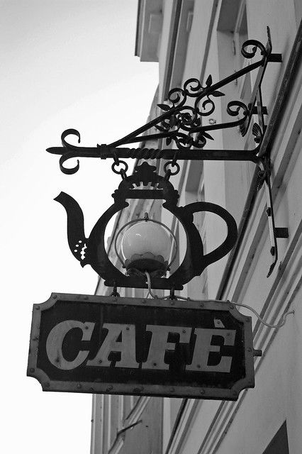 a black and white photo of a cafe sign hanging from the side of a building