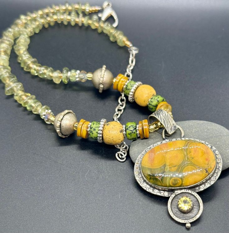 This necklace is stunning when worn!  The colors are marvelous and the jasper pendant shows you the pattern of yellow and green.  I beaded the necklace with shell, coconut, handmade beads from Thailand, Bali-styled round beads, and I spaced out the smooth peridot stones.  If you are looking for that special piece of jewelry, her it is  This necklace is 18 inches long and has an additional 5 inches of chain for adjusting the length. Artisan Yellow Gemstone Bead Necklaces, Artisan Yellow Gemstone Beaded Necklaces, Artisan Yellow Gemstone Beads Necklace, Yellow Necklaces With Natural Stones In Round Beads, Yellow Necklaces With Natural Stones And Round Beads, Yellow Necklaces With Natural Round Beads, Yellow Bohemian Beaded Pendant Necklace, Green I, Peridot Stone