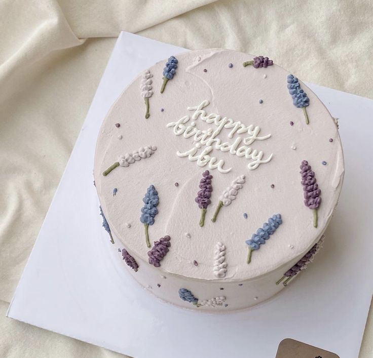 a white cake with purple flowers on it sitting on top of a card and envelope