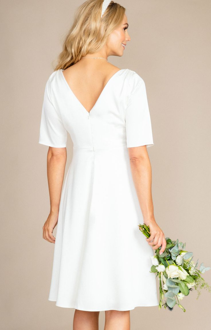 The Zoey maternity wedding dress is simple, refined and elegant.Heavyweight sheen satin has a gentle stretch making it sumptuous and comfortable to wear all day (and night) long. A cross over neckline features dramatic pleats from shoulder to waist. Elbow length sleeves and a knee length skirt create a fun and flirty finish to this sweet bridal style you will love. Add a touch of sparkle with one of our many decorative bridal sashes or choose a beautiful headband for playful glamour. Cross-over Elegant V-neck Bridal Dress, White Wedding Dress With Flattering Silhouette, Elegant Bridesmaid Wedding Dress With V-neck, Elegant Bridesmaid V-neck Wedding Dress, Elegant A-line Dress For Wedding Night, A-line Wedding Dress With Flattering Silhouette, Elegant A-line Wedding Dress For Bride, Elegant A-line Wedding Night Dress, Elegant V-neck Bride Dress