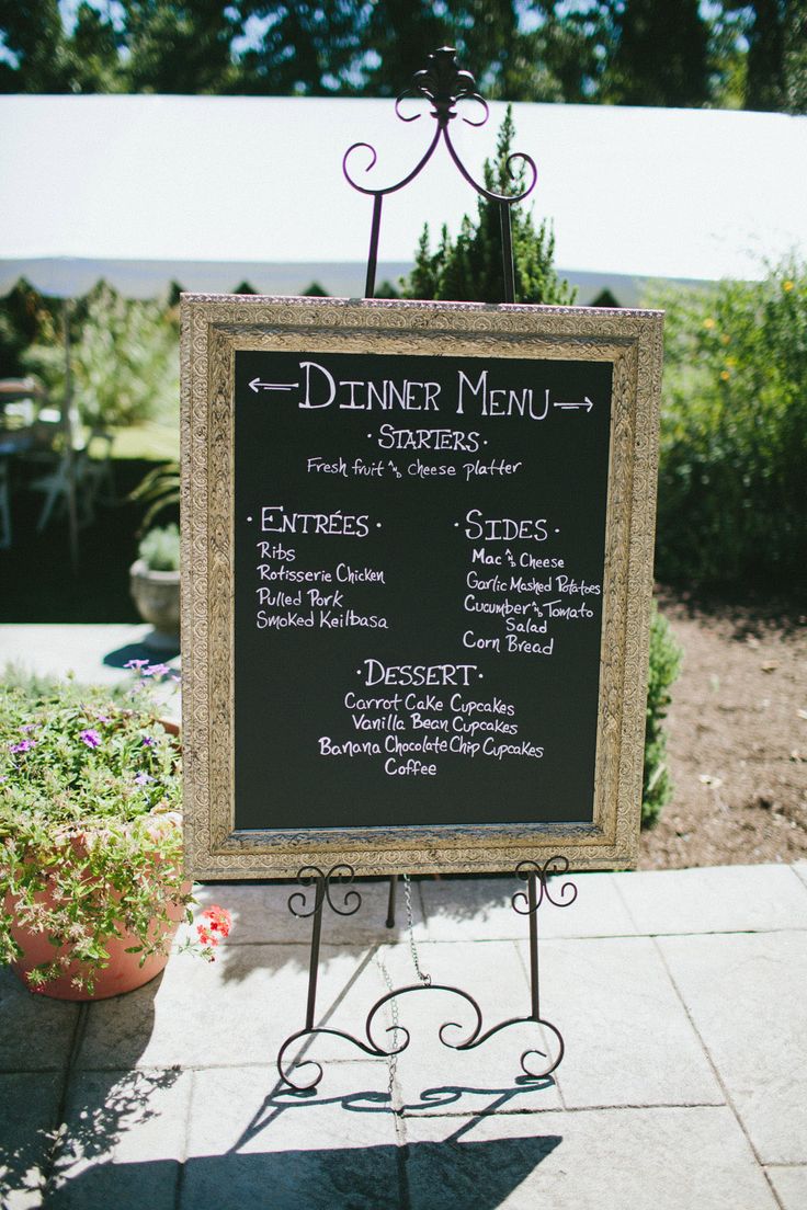 a menu sign sitting on top of a sidewalk next to potted plants and flowers