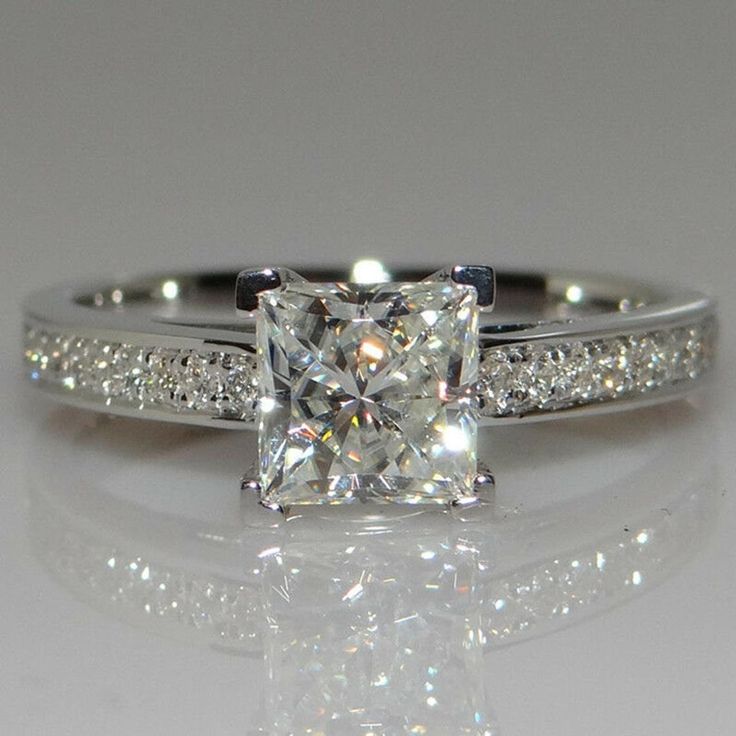 an engagement ring with a princess cut diamond in the center and side stones on each band