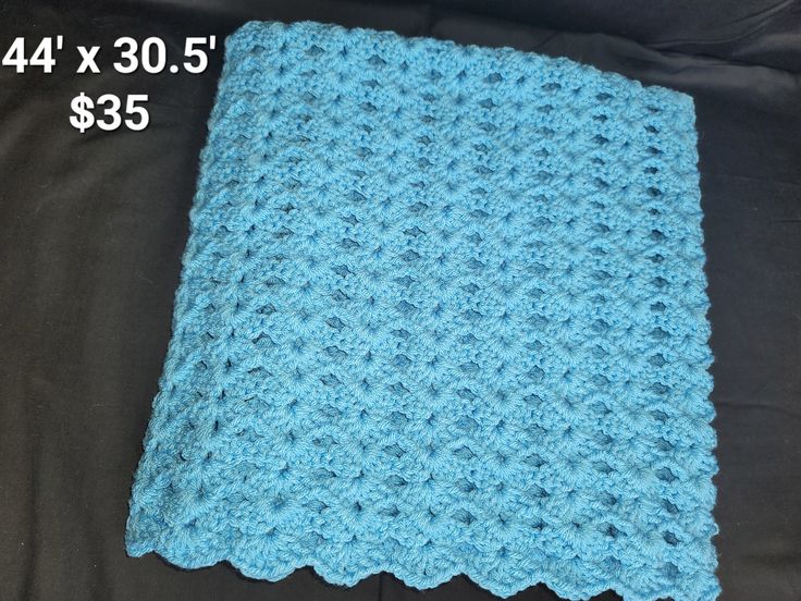 a blue crocheted blanket sitting on top of a black bed next to a pillow