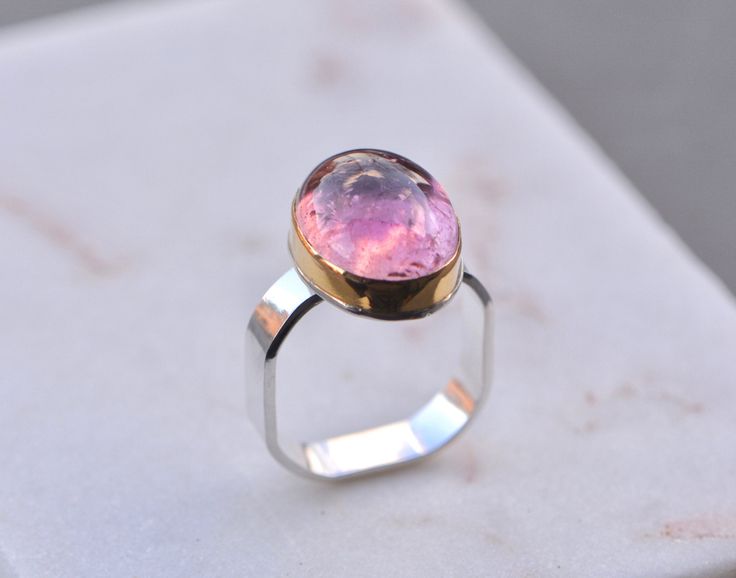 Metal: 925 Sterling Silver, 14k Gold Gemstone Type: 16 cts Natural Pink Tourmaline Gemstone Shape: Oval Cabochon Design Elements: 14k Gold Bezel Setting, Square band, Stock Ring Size: 105 Sizable: No This stunning ring is absolutely gorgeous to behold. The ring is hand-forged with a square band of sterling silver and 14k gold. It features a stunning natural pink tourmaline which has a lot of life. The band is approx 5mm wide and the ring is designed in a square comfort fit. Packaging : All produ Polished Tourmaline Ring As Gift, Polished Tourmaline Rings For Gift, Anniversary Tourmaline Rings With Polished Finish, Anniversary Rings With Polished Tourmaline, Mixed Metal Ring, October Birthstone Ring, Mixed Metal Rings, Ring Square, October Birthstone Rings