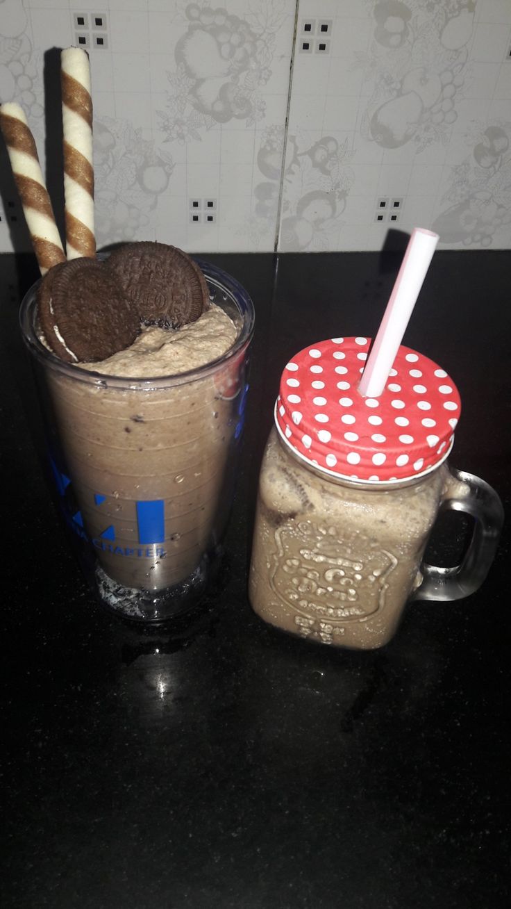 two glasses filled with chocolate milkshakes on top of a black table next to each other