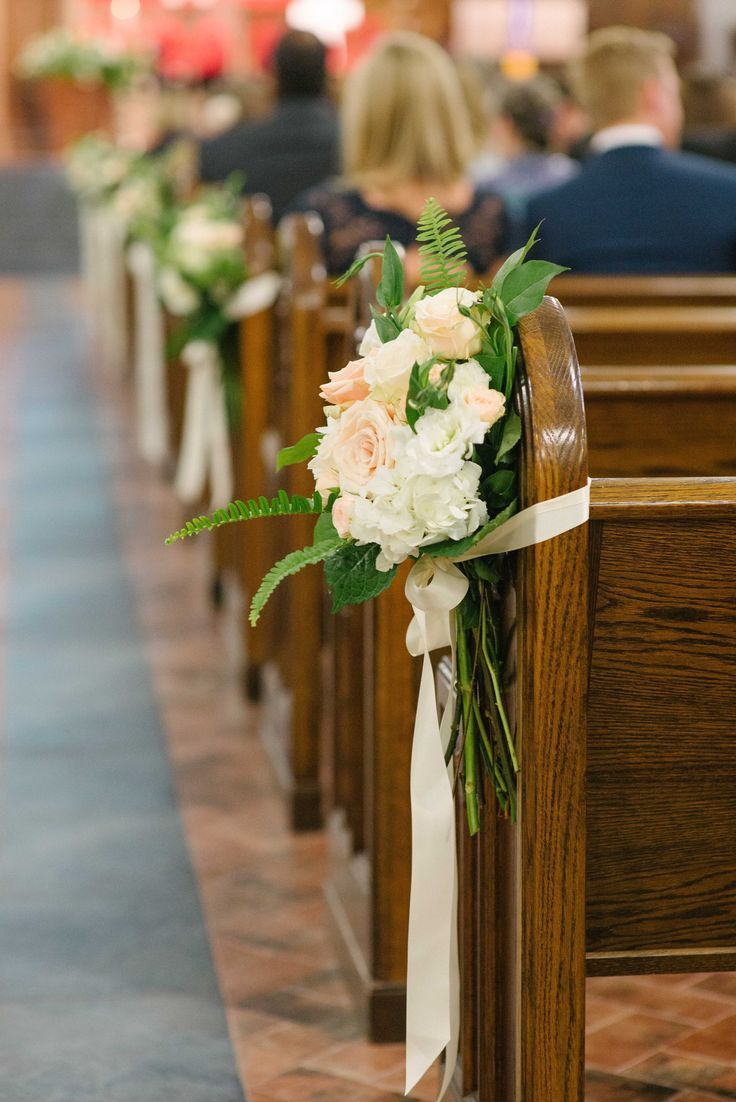 the aisle is lined with pews decorated with white and peach flowers, greenery, and ribbons