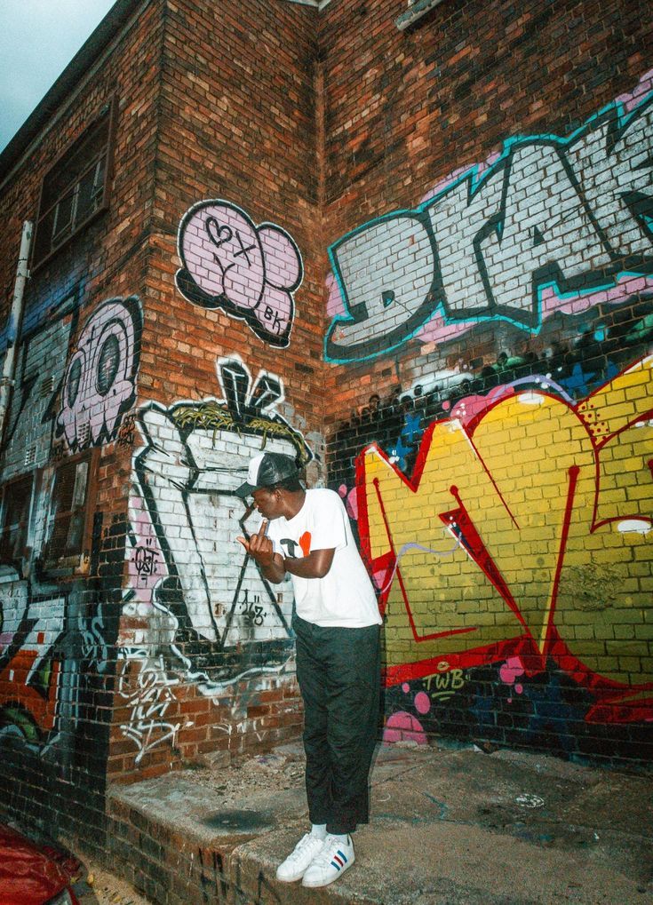 a man standing in front of a brick wall with graffiti on it and looking at his cell phone