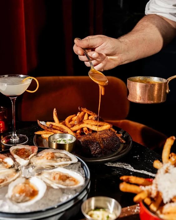 a person is pouring sauce on some oysters and french fries at a restaurant table