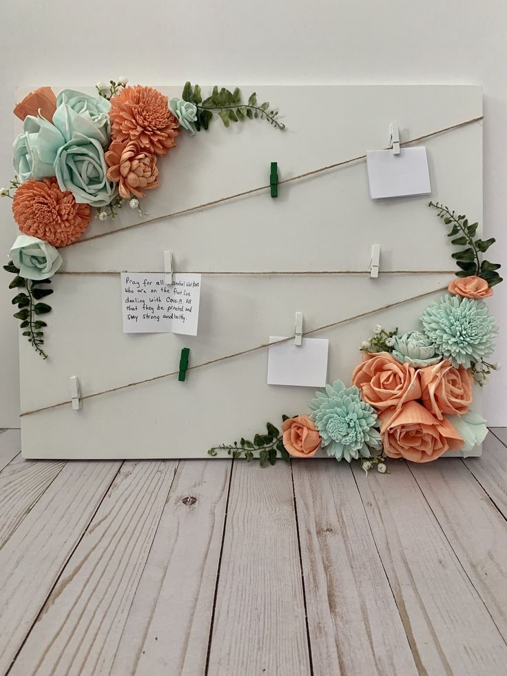 an arrangement of flowers on a white board with notes pinned to it and attached to clothes pins