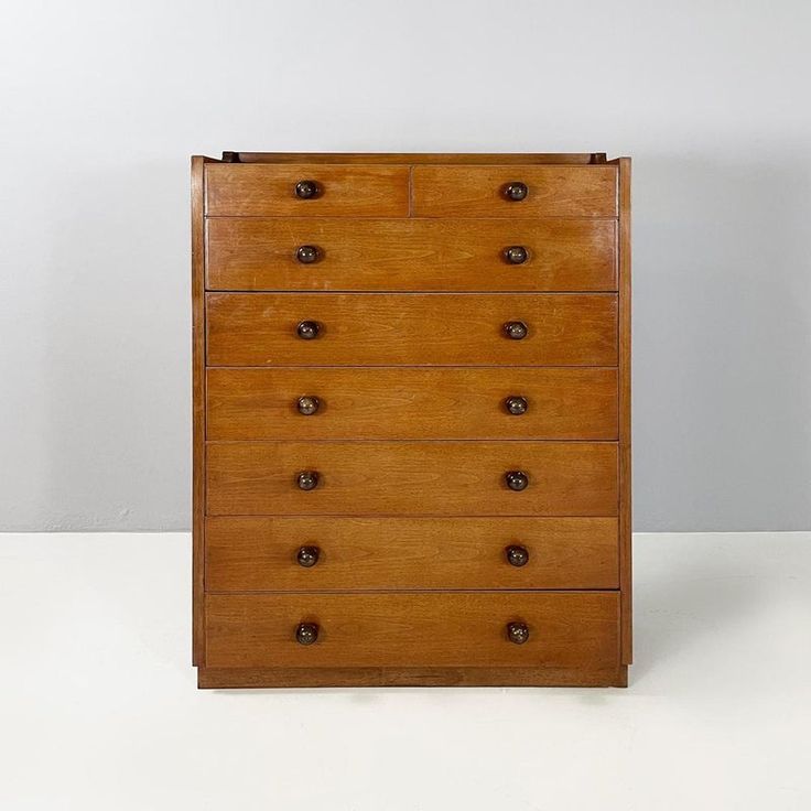 an old wooden dresser with many drawers and knobs on the bottom drawer, against a white wall