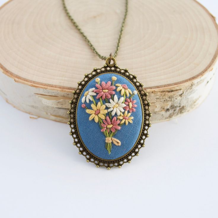 a necklace with flowers on it sitting next to a piece of wood and a white background