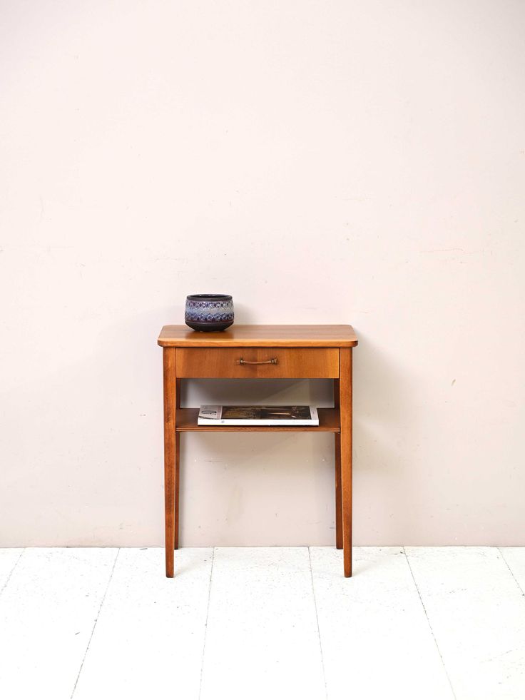 a wooden table with a blue vase on top of it next to a white wall