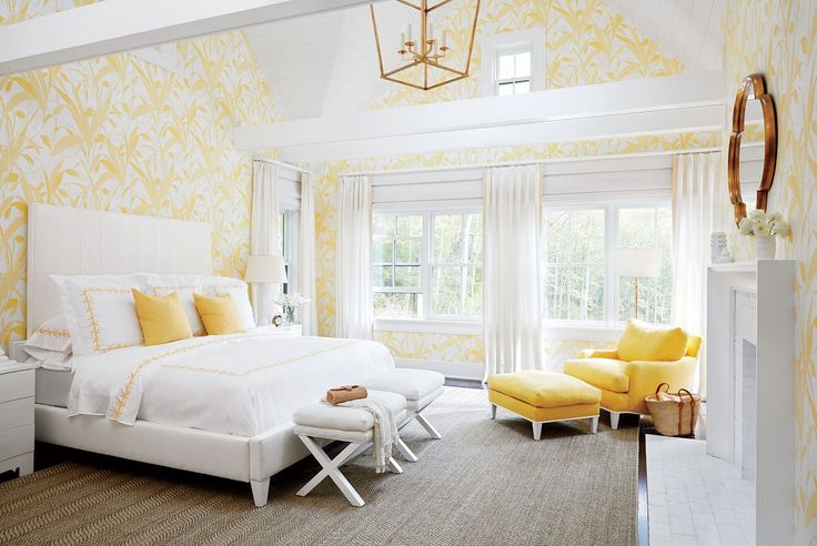 a bedroom decorated in yellow and white with a large bed, two chairs, windows, and a chandelier