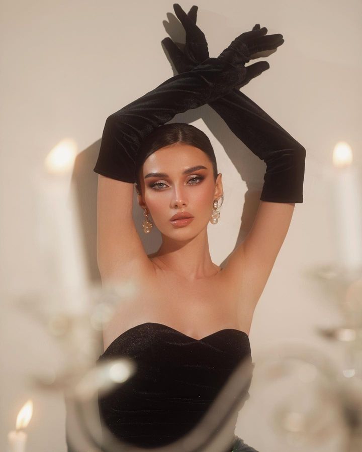 a woman in a black dress is holding her hands up above her head and looking at the camera