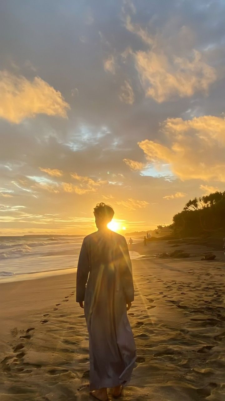 a man standing on top of a sandy beach next to the ocean under a cloudy sky