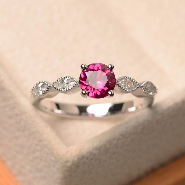 a pink ring sitting on top of a wooden table next to a white cloth covered box