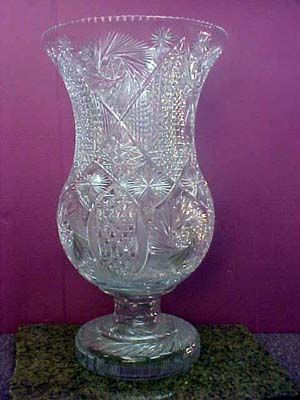 a clear glass vase sitting on top of a green table next to a purple wall