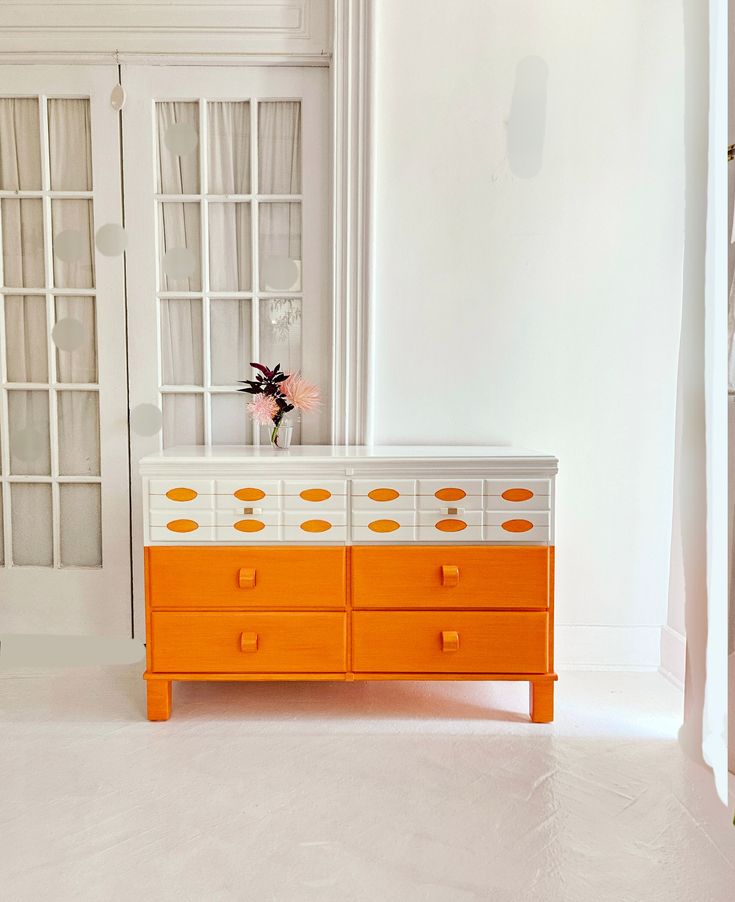 an orange and white dresser with flowers on top