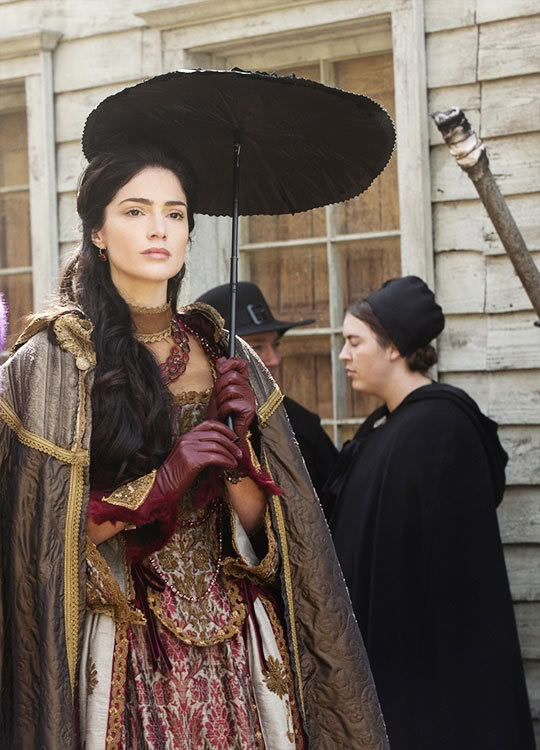 a woman dressed in medieval clothing holding an umbrella and looking at the camera with other people behind her