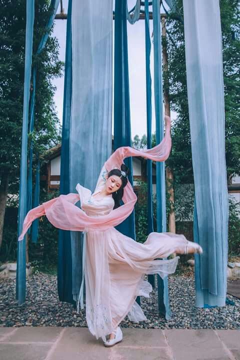 a woman in a white dress and pink scarf is posing for the camera with her arms outstretched