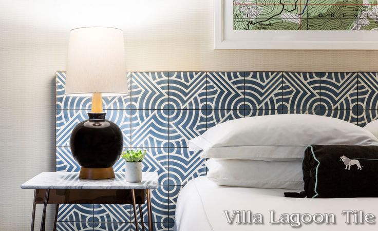 a bed with white sheets and blue patterned headboard next to a night stand with a lamp on it