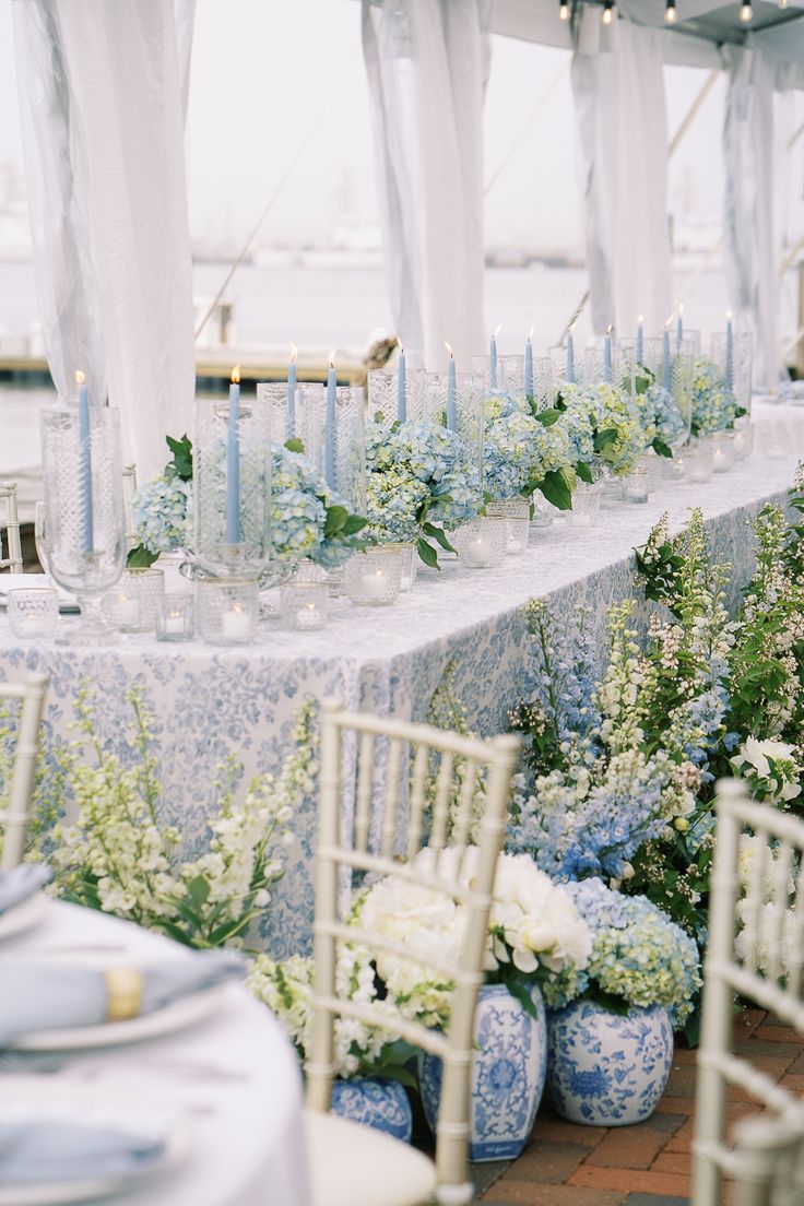 a table with blue and white vases filled with flowers next to candles on top of it