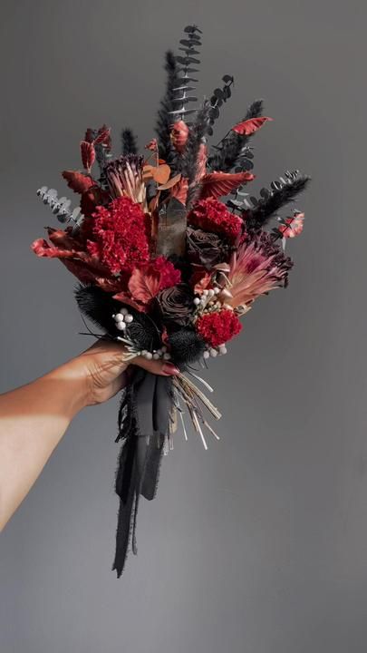 a person holding a bouquet of flowers in their left hand, against a gray background