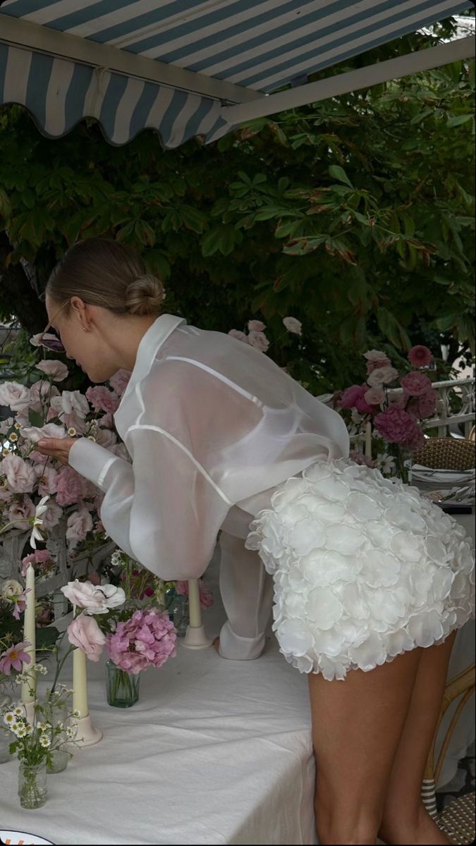 a woman in white dress standing over a table with flowers