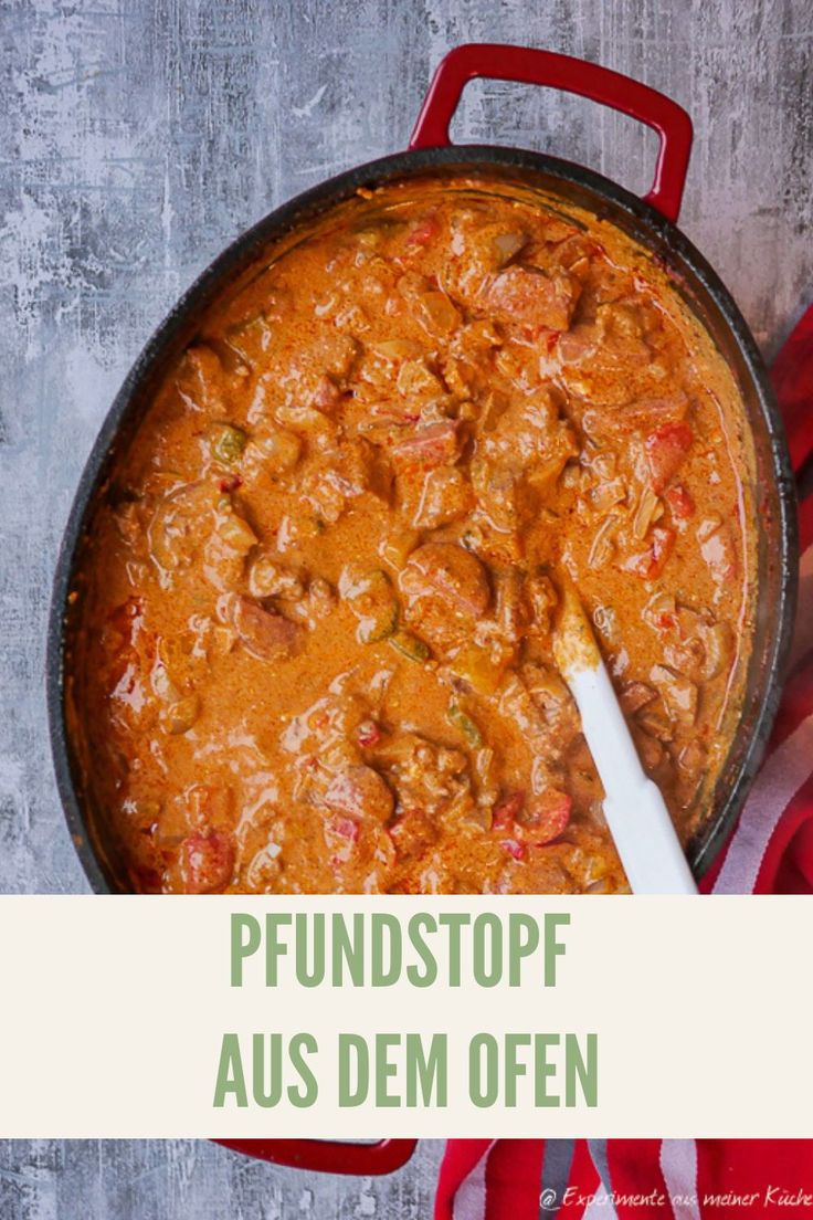 a red pot filled with stew next to a white spoon on top of a table