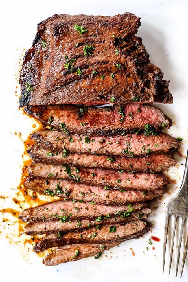 sliced steak on a white plate with a fork and parsley garnished in seasoning