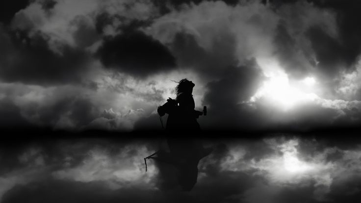 the silhouette of a person sitting on a bench in front of clouds