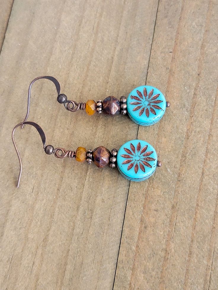 These rustic Czech glass bead dangle earrings feature copper accents and a combination of burnt orange and rustic brown colors. The addition of turquoise aster coin beads, washed in bronze, adds a unique touch to these earrings. Perfect for adding a touch of Bohemian charm to any outfit. Czech glass beads Copper accents Copper ear hooks Length 1.75" Created in studio - Wilmington, NC Cheap Bohemian Beaded Dangle Earrings, Cheap Bohemian Spring Jewelry, Cheap Czech Glass Beaded Earrings With Round Beads, Cheap Vintage Czech Glass Beaded Earrings, Cheap Wire Wrapped Czech Glass Earrings, Cheap Czech Glass Jewelry With Polished Beads, Cheap Bohemian Glass Jewelry, Cheap Czech Glass Dangle Earrings, Cheap Artisan Jewelry With Czech Glass