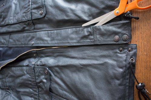 an orange pair of scissors sitting on top of a black leather jacket with zippers