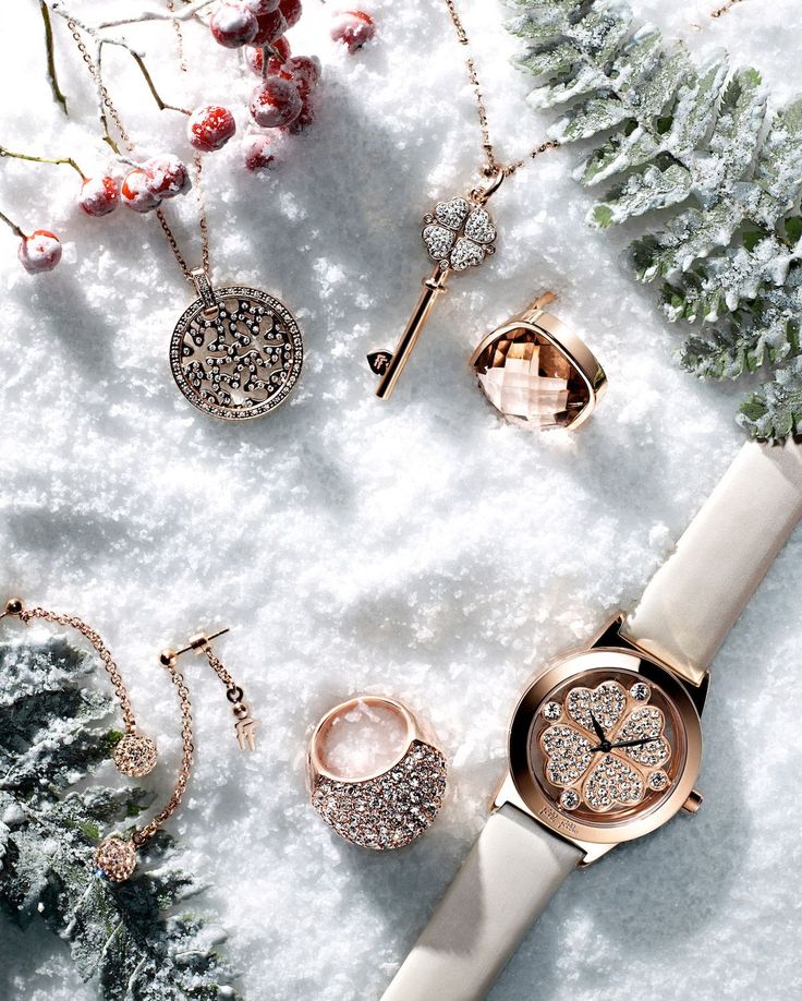 several different watches and necklaces laying in the snow next to some christmas tree branches