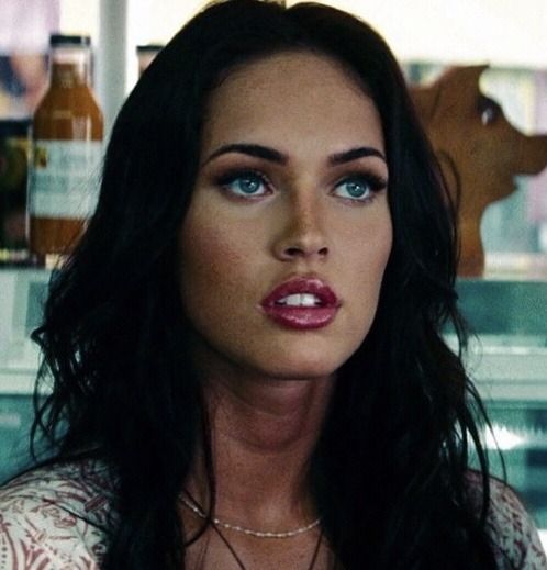 a woman with long black hair and blue eyes wearing a necklace in front of a counter