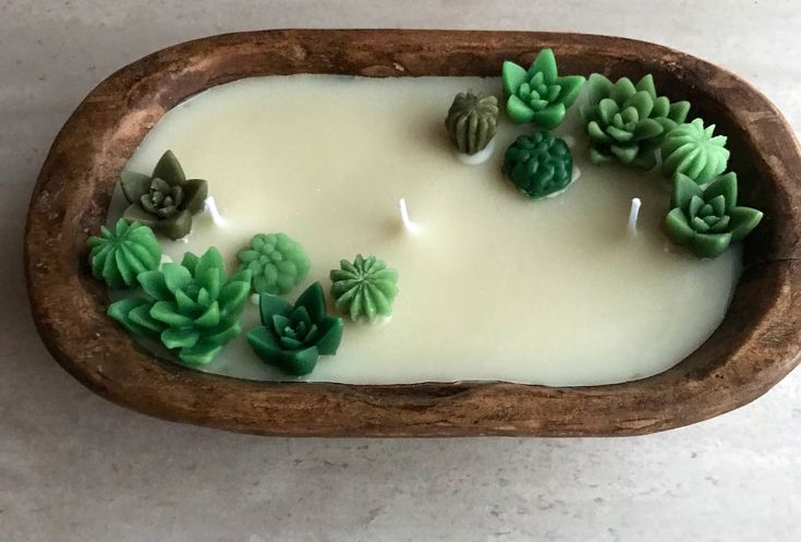 a wooden bowl filled with green plants on top of a white countertop next to a candle