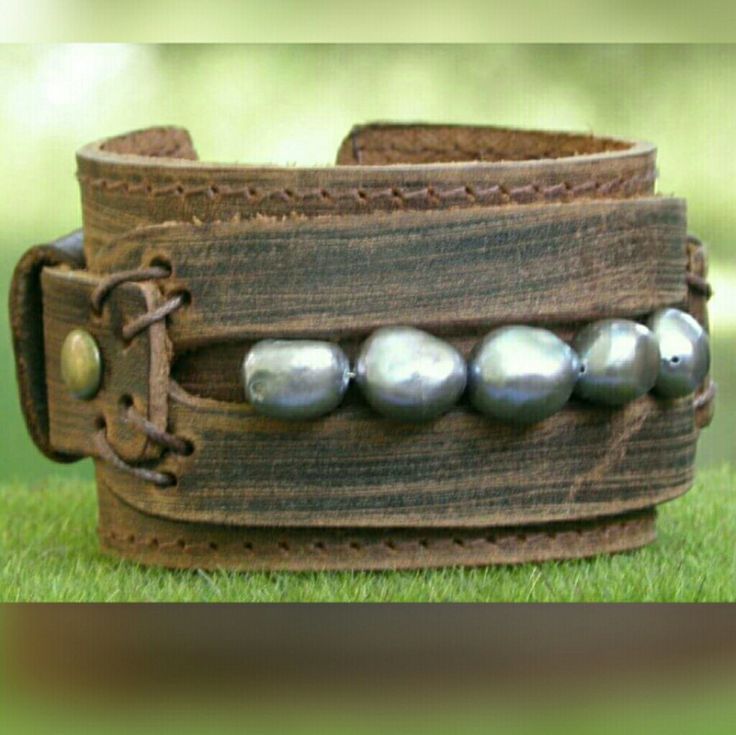 a leather bracelet with metal beads on top of it in the middle of some grass