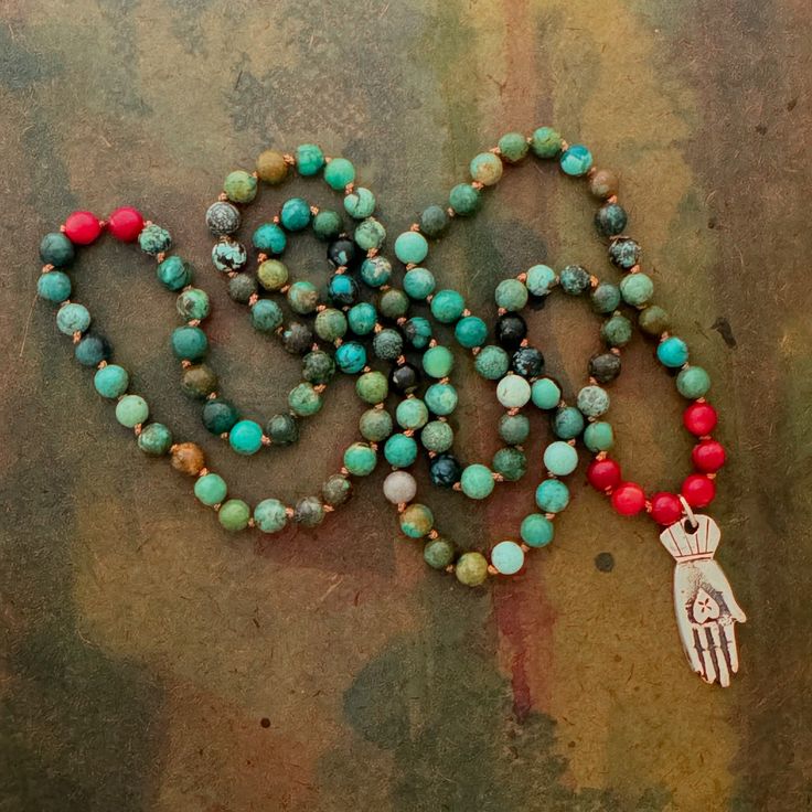 This Mala necklace has the auspicious number of 108 beads on a silk cord. Each bead is hand knotted in between and are all approximately 6mm New Mexican turquoise beads and 8 natural coral beads. The mala hangs at 16 inches and can also  be wrapped around the wrist 4 times.  Turquoise is the stone of wholeness. It is balancing and induces a sense of serenity and peace. It can help restore depleted vitality and lift sagging spirits. This stone has the capacity to heal the emotional body, relieve stress, and bring the focal point of awareness to its proper center of the heart. "The heart in the hand" Mexican silver Milagros hand made in Taos New Mexico.  This Milagros is widely considered to symbolize charity, or to mean something is "from the heart". It represents friendship, love and truth Adjustable Beaded Turquoise Necklace For Meditation, Bohemian Mala With 8mm Beads For Blessing, Bohemian Turquoise Necklace With 108 Beads For Gift, Adjustable Spiritual Turquoise Necklace For Meditation, Artisan Chrysocolla Beaded Necklace For Healing, Artisan Hand Knotted Necklace For Gift, Artisan Hand Knotted Jewelry As A Gift, Artisan Hand Knotted Jewelry For Gifts, Artisan Hand-knotted Jewelry For Gifts