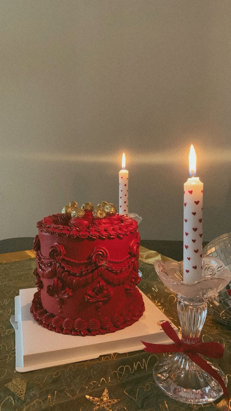 a red cake sitting on top of a table next to two lit candles