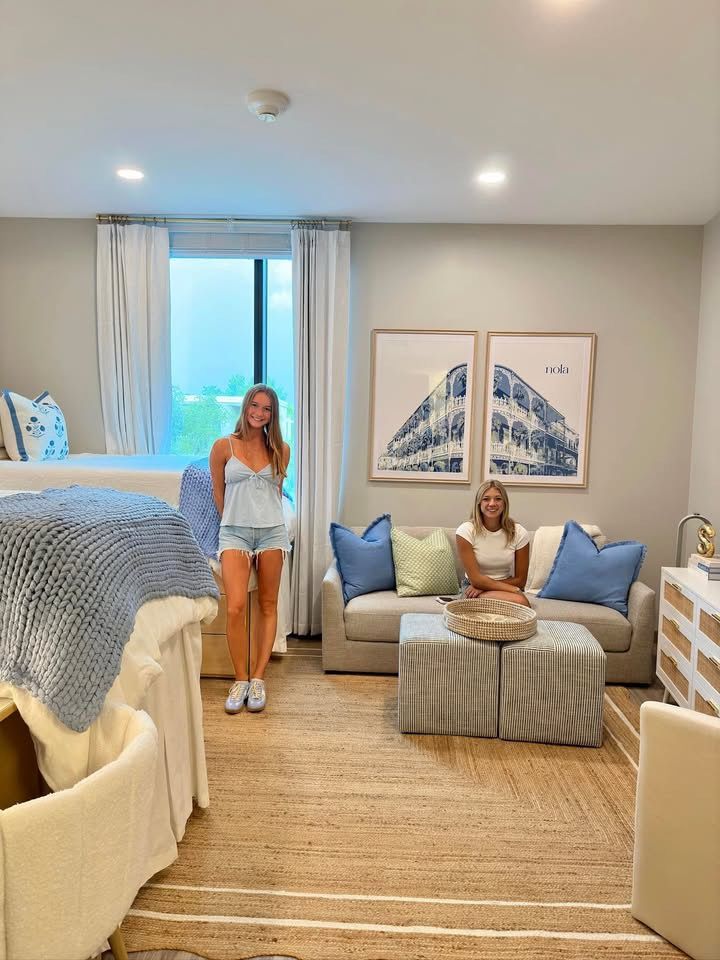 a woman sitting on a couch in a bedroom next to a bed with blue and white pillows