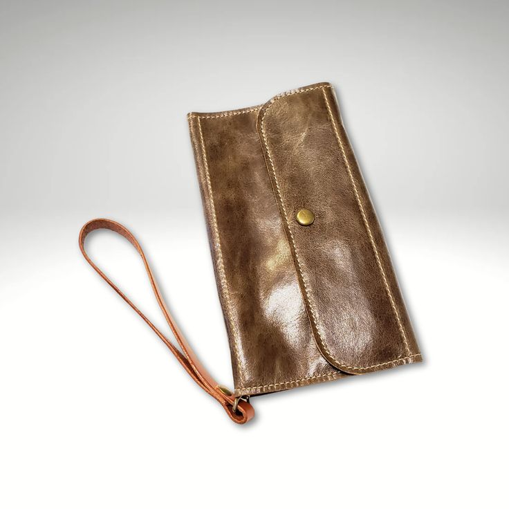 This clutch style wallet is versatile, changing from a clutch to a wristlet by detaching the strap, or tuck the strap inside to keep it out of the way. Two card slots inside, plus 2 zipper pockets and a bill pocket in the back. Magnetic snaps keep the pockets attached together and also closes the top flap. Body is a supple cognac brown color, with a firmer field tan leather wristlet strap. Size approx. 8" wide x 4.25" high when folded. Pattern is Essentials Leather Wallet by Georgia Girl Stitche Handheld Wallets With Card Slots For Daily Use, Classic Pouch Clutch With Card Slots, Travel Clutch Wallet With Interior Card Slots, Bifold Clutch With Interior Card Slots For Daily Use, Handheld Wallet With Card Slots For Daily Use, Travel Bifold Coin Purse With Snap Closure, Everyday Rectangular Trifold Wallet With Coin Pocket, Trifold Wallet With Cell Phone Pocket, Rectangular Wallets With Interior Card Slots For Everyday Use