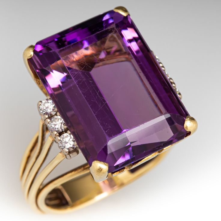 This stunning ring is centered with one (1) emerald cut natural amethyst set into a four-prong setting. The center stone is flanked to each side with a row of three (3) prong set, round brilliant cut diamonds. The ring measures 18.2mm at the top, rises 10.2mm above the finger, tapering to 4.0mm wide and 1.5mm thick at the base of the shank. It is currently a size 7.5. Vintage Amethyst Rings, Cocktail Diamond Ring, Amethyst Rings, Amethyst Cocktail Ring, Amethyst Ring Vintage, Gold Amethyst Ring, Amethyst Set, Colored Stone Rings, Vintage Cocktail Ring