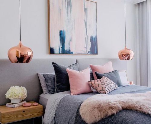 a bedroom with pink and grey decor on the walls, gray bedding, white pillows, and gold accents