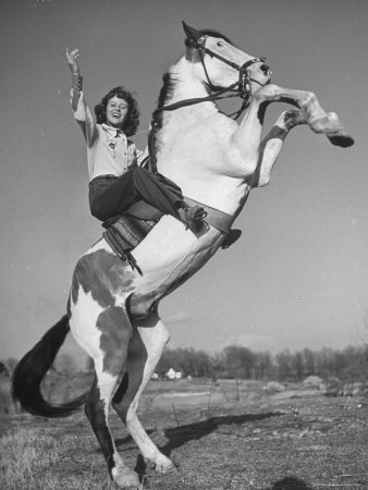 a woman riding on the back of a white and brown horse in an open field