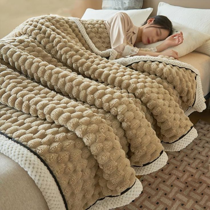 a woman laying on top of a bed covered in a blanket and sleeping next to pillows