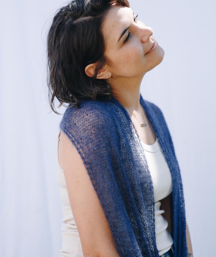 a woman with her eyes closed wearing a blue shawl over her shoulder and looking up