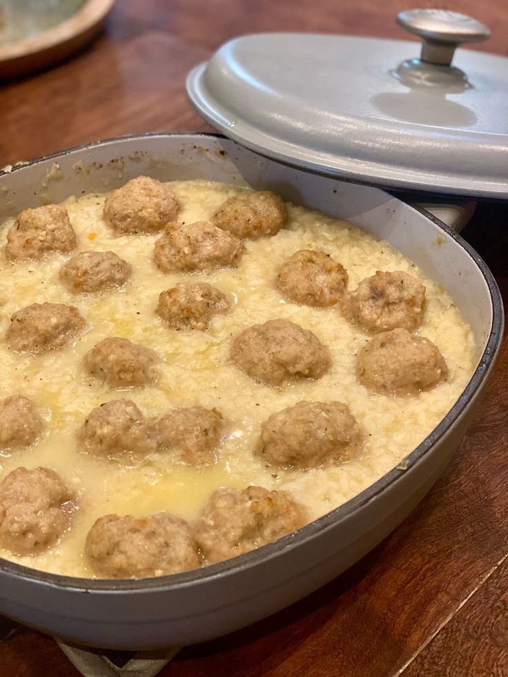 a pan filled with meatballs and cheese on top of a wooden table next to a casserole dish