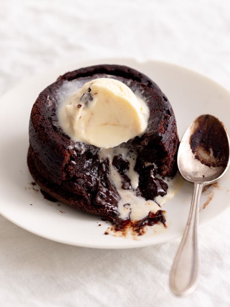 a chocolate dessert on a plate with ice cream in the center and spoon next to it