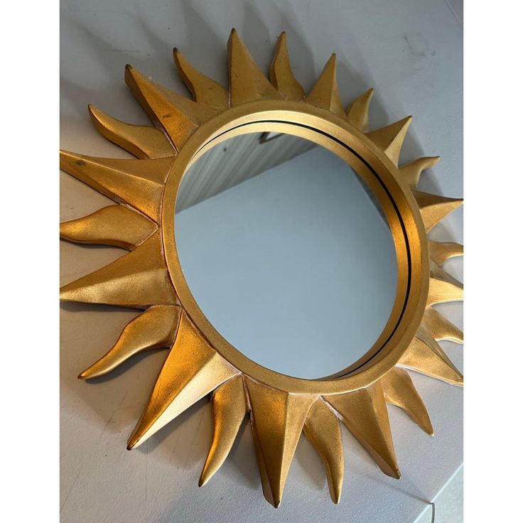 a gold sun shaped mirror sitting on top of a white counter next to a wall